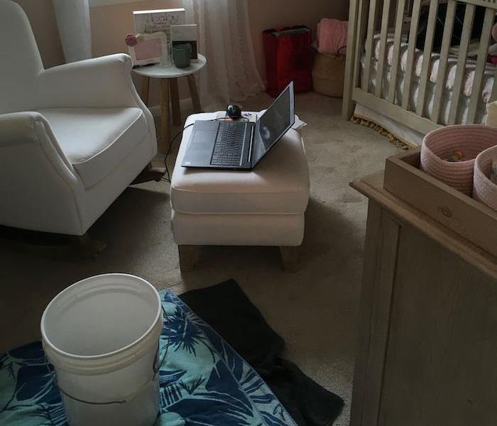 Room with chair and crib with bucket on towels on the floor
